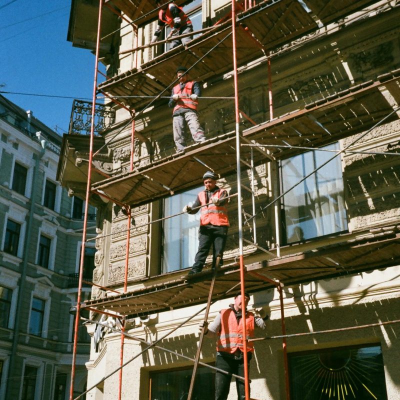 Construction workers on scaffolding renovating a building facade on a sunny day.